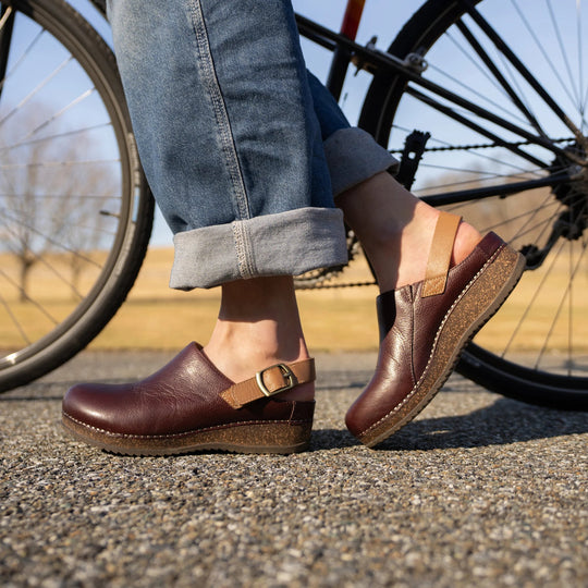 Brown leather clogs with ankle straps and cork wedge soles worn with cuffed jeans