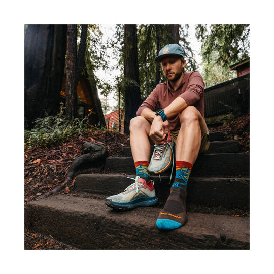 Light gray trail running shoes with coral heels and teal accents, shown with colorful hiking socks.