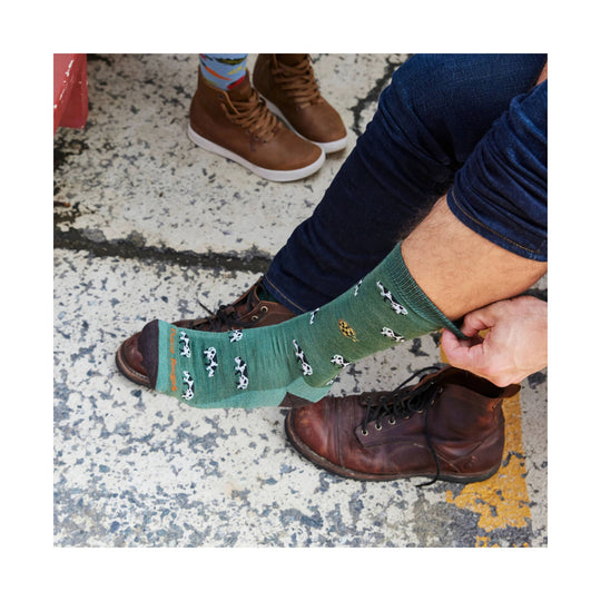 Green crew sock with cow pattern and orange logo text on the foot
