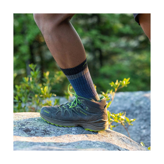 Low-cut hiking shoe with green laces and sole on a rocky trail, shown on a person’s foot