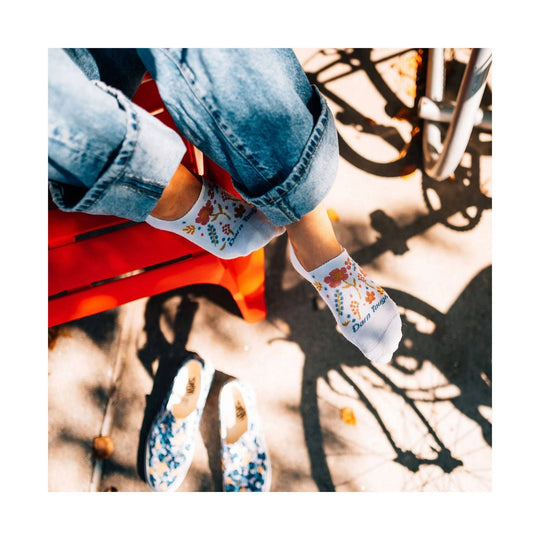 White no-show socks with colorful floral pattern and visible Darn Tough text, worn with jeans and floral slip-ons