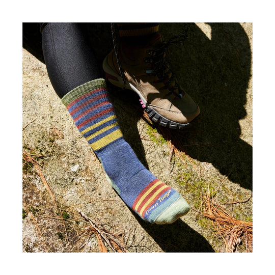 Striped knee-high wool hiking sock with blue, green, red, and yellow bands, worn with a tan hiking boot