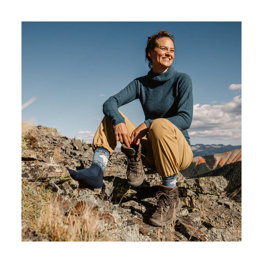 Blue patterned boot socks worn with hiking boots on a woman sitting on rocks