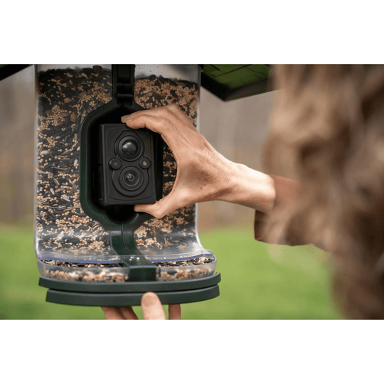 Smart bird feeder with built-in camera being held and adjusted by hands outdoors