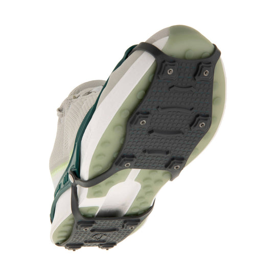 Traction device with black metal spikes, green rubber harness, and a white-and-gray strap shown from below