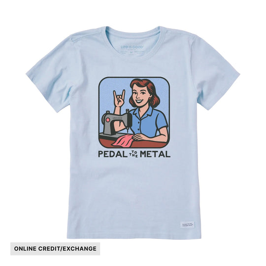 Light blue short-sleeve T-shirt with a retro woman at a sewing machine and the text "PEDAL TO THE METAL"