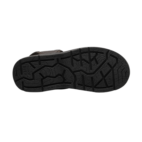 Black outsole of a closed-toe sandal with deep tread and brown upper visible at the edge