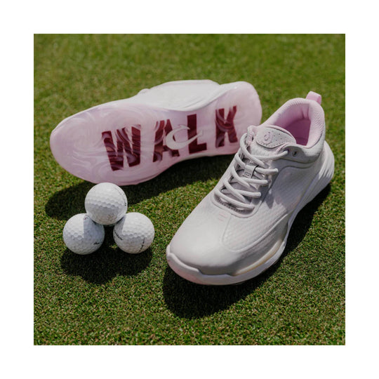 White golf shoes on grass, one showing a pink sole with WALK text, alongside golf balls