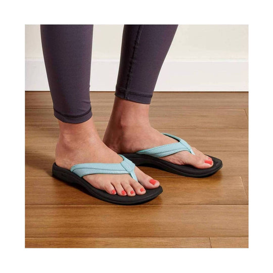 Light blue thong sandals with black soles worn with dark leggings on a hardwood floor