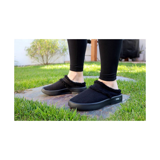 Black slip-on mule slippers with fuzzy trim and thick soles, shown on grass