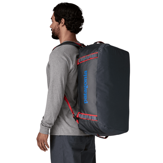 Dark duffel bag backpack worn on a person’s back with red straps and blue vertical branding