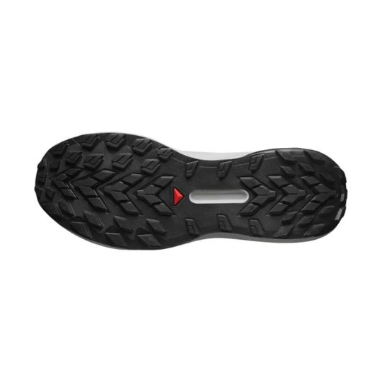Black trail shoe outsole with aggressive lugs and a red triangular accent
