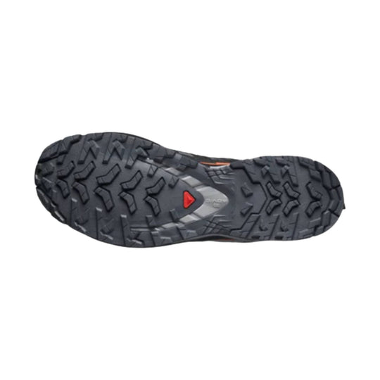 Black trail shoe outsole with rugged multi-directional lugs and a red triangular logo at the center