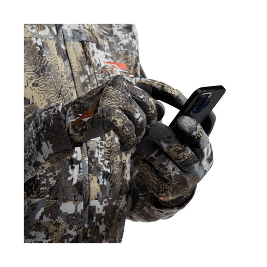 Camouflage insulated gloves holding a smartphone in front of a matching camo jacket