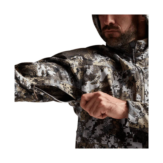 Man wearing a pixel-camo hooded jacket with a full front zipper and chest pocket, shown pulling at the sleeve