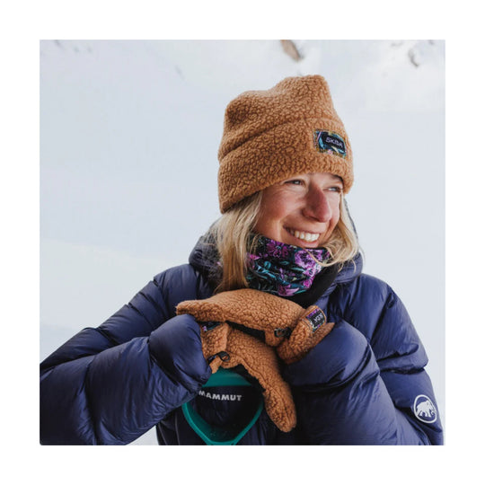 Brown fleece neck warmer with a black Skida patch, worn with winter gloves and a navy puffer jacket