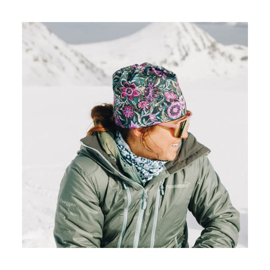 Floral patterned winter hat worn with mirrored ski goggles and an olive-green jacket in snowy mountains