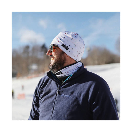 White patterned beanie with matching neck gaiter, worn with sunglasses and a dark fleece jacket