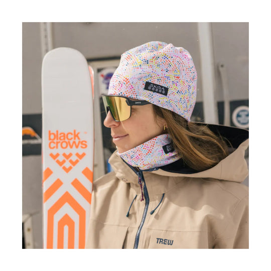 Multicolor dotted knit beanie with matching neck gaiter, worn with ski goggles and a beige jacket