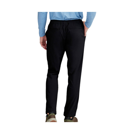 Black athletic pants shown from the back on a model, with elastic waistband and zip pockets