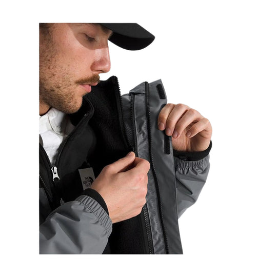 Man wearing a black and gray zip-up jacket, shown in profile while opening the front flap