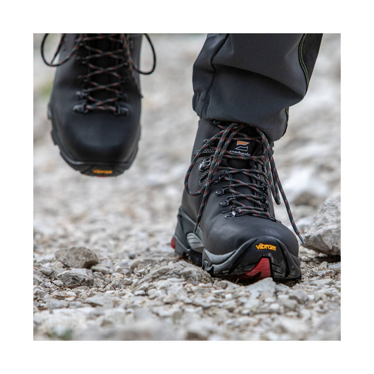 Black leather hiking boots with red-and-gray laces and Vibram soles, shown walking on rocky ground
