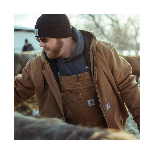 Brown insulated work jacket over brown bib overalls, worn with a black beanie and sunglasses.