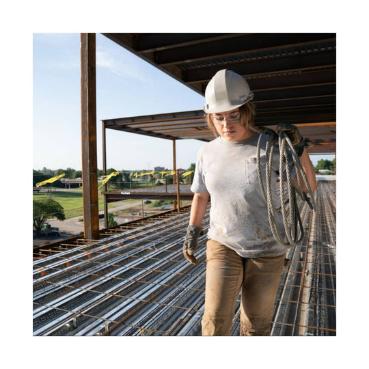 Woman on a construction site wearing a heather gray pocket T-shirt, hard hat, and work gloves, carrying coiled rope