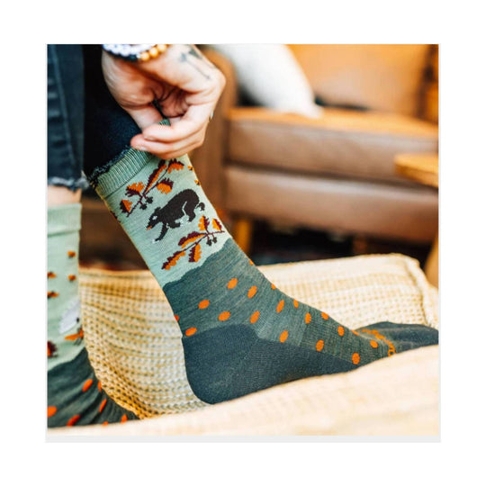 Green crew sock with orange dots and black wildlife pattern being worn indoors