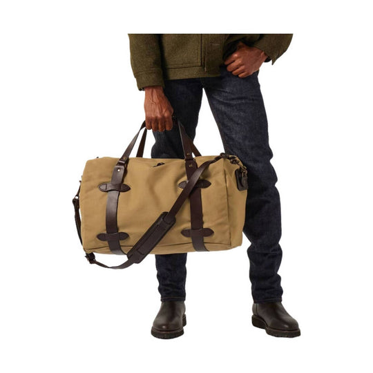 Tan canvas duffel bag with dark leather straps, shoulder strap, and buckle closures
