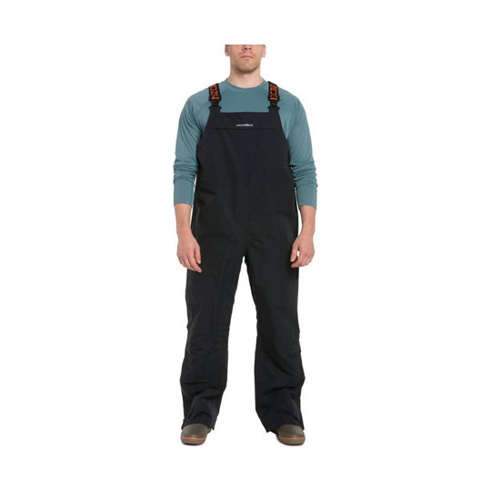 Black bib overalls with shoulder straps worn over a teal long-sleeve shirt
