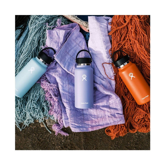 Three insulated water bottles in light blue, lavender, and orange on textured blankets