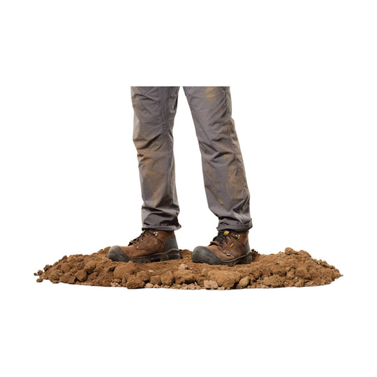 Brown leather work boots on muddy ground, shown from the lower legs down