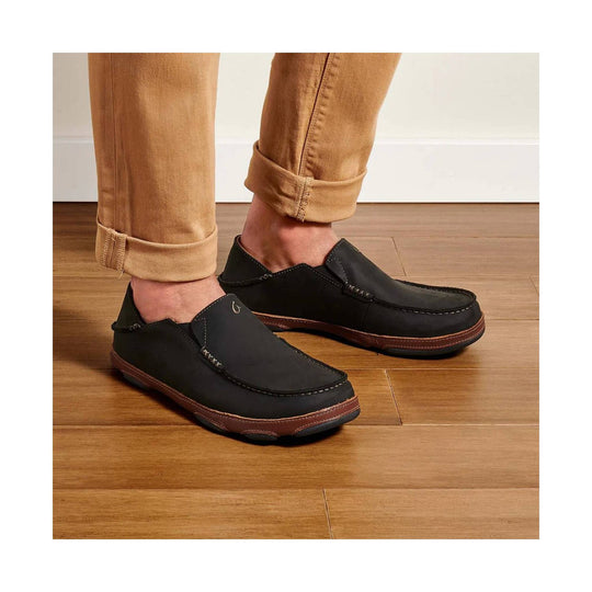 Black slip-on loafers with brown stitched soles, shown on tan rolled-cuff pants indoors