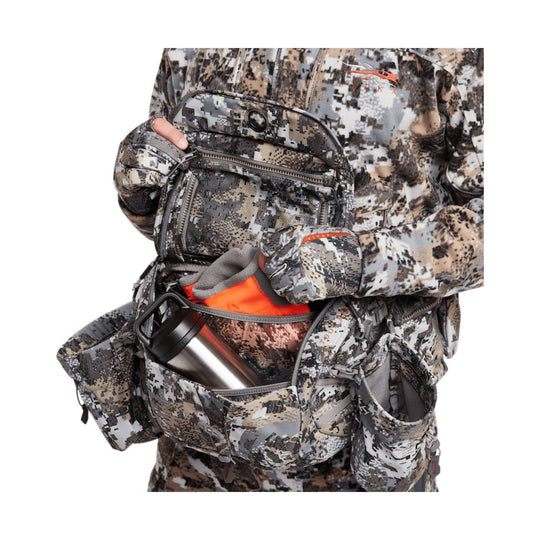 Camouflage chest and waist pack with multiple zippered pockets and a stainless steel bottle in the front pocket