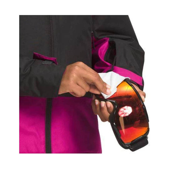 Black and pink insulated jacket with a sleeve pocket holding orange ski goggles