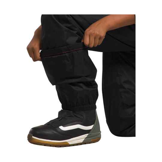 Black insulated snow pants cuff being adjusted above a black winter boot