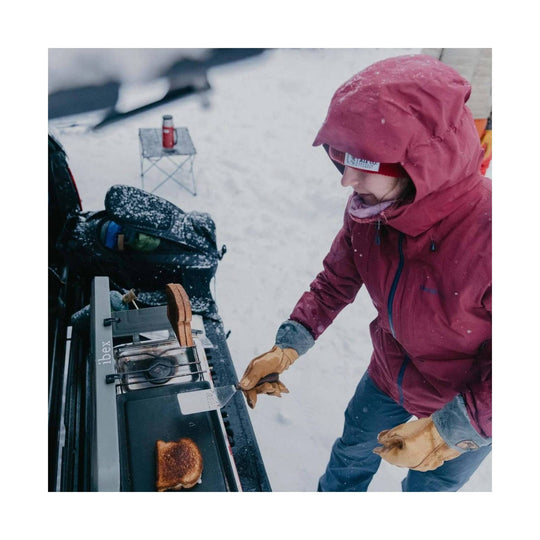 Tan leather insulated gloves worn by a person cooking outdoors in the snow